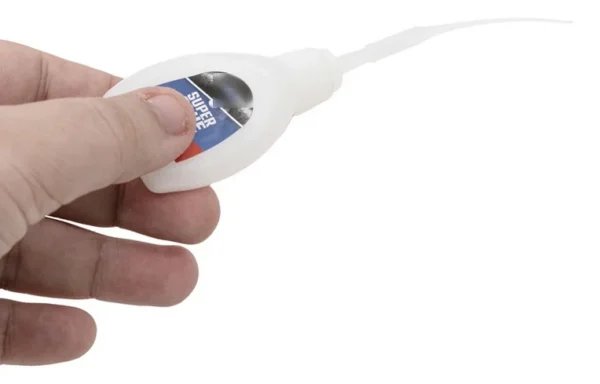 Flacon de colle cyanoacrylate tenu en main, canule fine montée sur le col