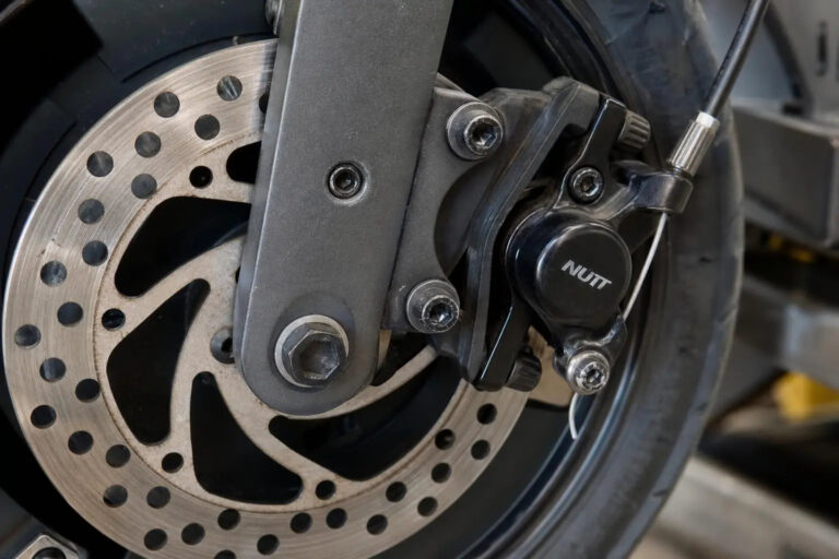 Frein trottinette électrique: дисque et étrier de frein à disque montés sur la roue arrière, avec disque perforé et étrier noir.