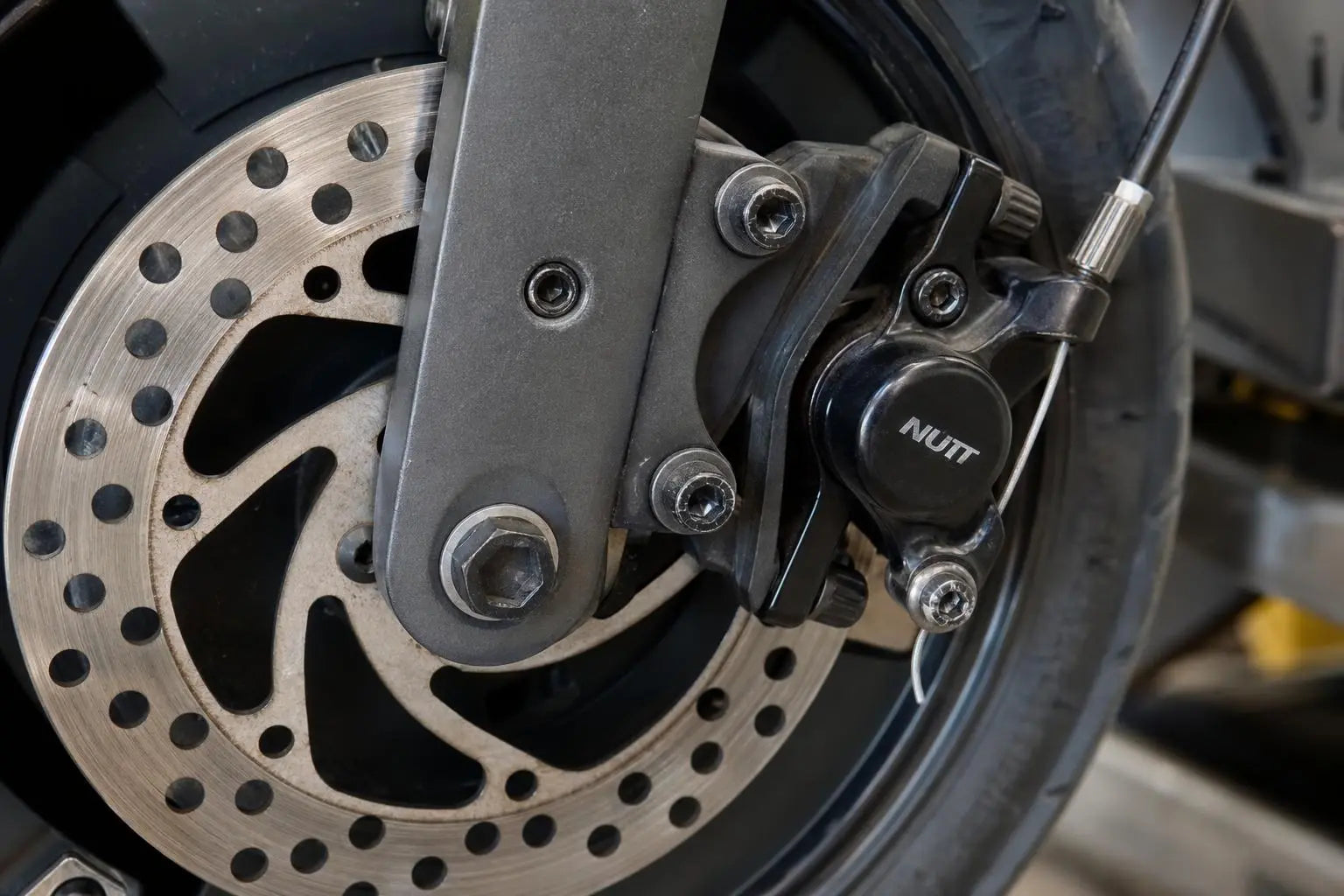 Frein trottinette électrique: дисque et étrier de frein à disque montés sur la roue arrière, avec disque perforé et étrier noir.
