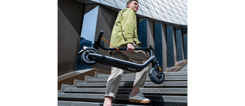 Trottinette électrique Ninebot E2 E II pliée et portée à la main dans un escalier
