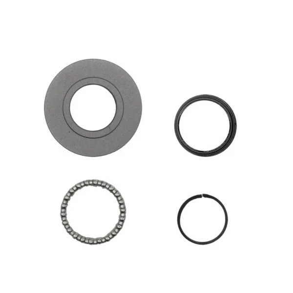 Les quatre éléments du jeu de direction posés à plat : disque plat gris, joint noir, cage à billes et jonc fendu